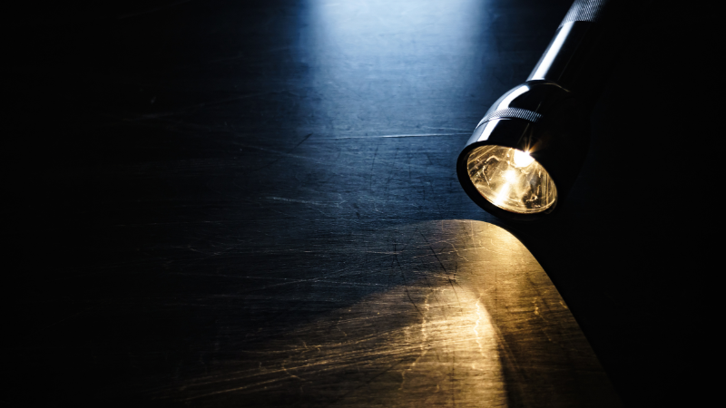 Päällä oleva taskulamppu pöydällä pimeässä.